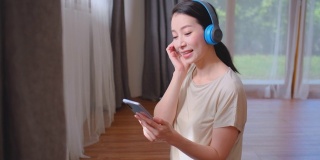 美女在客厅用蓝牙耳机在晨光下听手机里的音乐。待在家里的观念和应用良好的活动预防冠状病毒感染