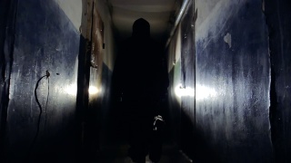 穿着黑色夹克，背着包的匪徒沿着走廊离开摄像头视频素材模板下载