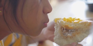 亚洲女孩在家窗前吃玉米蛋黄酱包(玉米面包)，慢镜头。