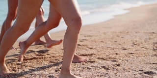 苗条的女性腿和脚走出海浪在沙滩上。漂亮女人喜欢去海边。水和泡沫的飞溅在120帧/秒的慢动作。女孩们在海里洗完澡后就去海边