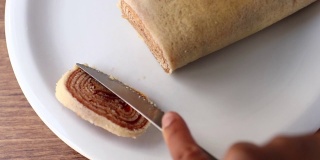 在切罗洛之火。将巴西甜点Bolo de Rolo(瑞士卷，卷饼)切成薄片，放在白色的盘子上，以木材为背景