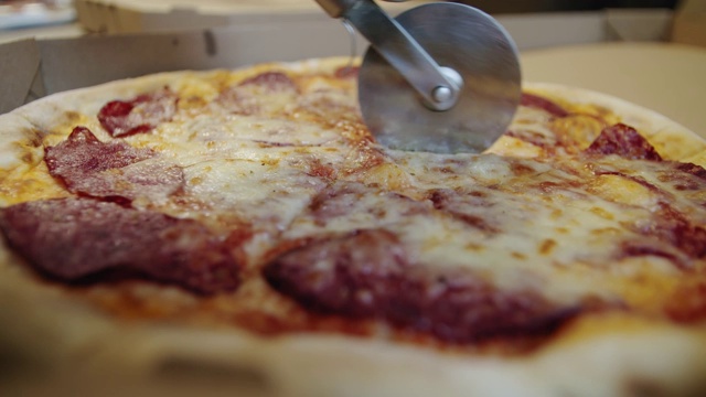 一个人用披萨刀把披萨切成多片的慢动作。特写镜头。