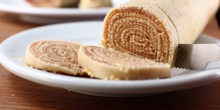 在切罗洛之火。将巴西甜点Bolo de Rolo(瑞士卷，卷饼)切成薄片，放在白色的盘子上，以木材为背景