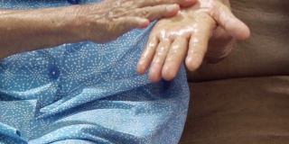 老年妇女使用护工提供的洗手液以帮助预防冠状病毒感染