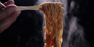 筷子美味面条与蒸汽和烟在黑暗的背景慢动作，亚洲餐的特写，热食物和快餐的概念