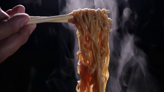 筷子美味面条与蒸汽和烟在黑暗的背景慢动作，亚洲餐的特写，热食物和快餐的概念视频素材模板下载