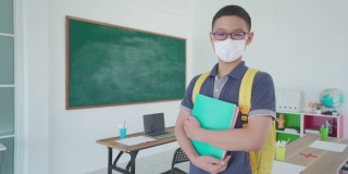 亚洲小学生男孩背着书包和书本戴上口罩，防止Covid - 19在教室里爆发，返校时重新开学，新常态的教育理念。