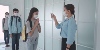 亚洲女教师在学生返校时使用体温计检查学生体温，以防止COVID-19的传播，新常态和教育理念。