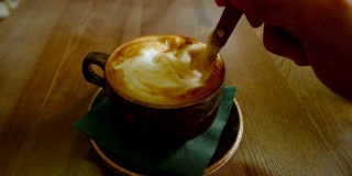 一个男人在杯子里搅拌卡布奇诺咖啡