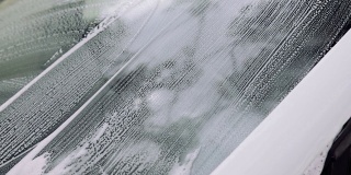男人的手用海绵和泡沫擦洗汽车的挡风玻璃。汽车服务理念