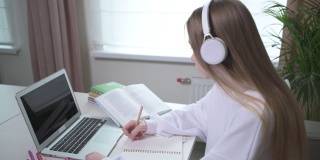 戴着无线耳机的女孩在一个空笔记本上写一篇演讲。