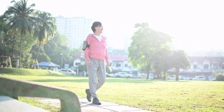 一位华裔老年妇女在公园晨练，在人行道上跑步