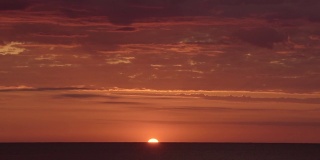 在明亮的红色和橙色的日落上，太阳在海洋的后面，很少有云