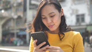 一名身穿黄色衬衫的日本妇女在街道附近使用智能手机视频素材模板下载