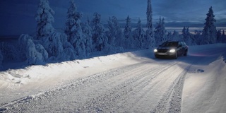 在拉普兰地区，一辆大灯车在夜晚被雪覆盖的路上行驶。采用针