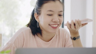 亚洲商务女性在家工作，桌上放着智能手机和笔记本电脑，心情愉快。社会距离的概念，以阻止冠状病毒疾病的传播。4 k UHD。缓慢的运动。视频素材模板下载