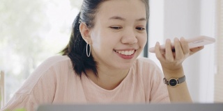 亚洲商务女性在家工作，桌上放着智能手机和笔记本电脑，心情愉快。社会距离的概念，以阻止冠状病毒疾病的传播。4 k UHD。缓慢的运动。