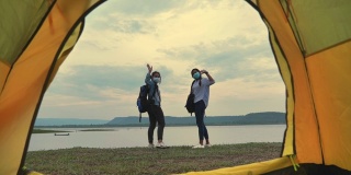 两个亚洲女背包客戴着面罩在湖边欣赏夏日日落的慢镜头。他们是快乐的，有乐趣的假期，放松的时刻。青少年自然户外日常生活的概念