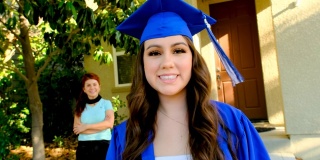 Young hispanic woman posing celebrating her graduation with her mother in the background