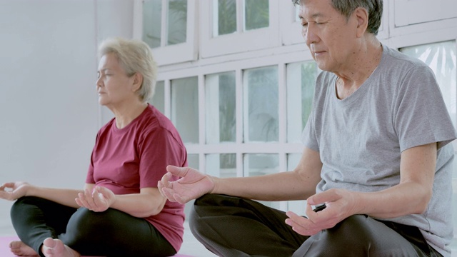 亚洲老年夫妇做冥想瑜伽在家锻炼。采购产品家庭，生活方式，人，老年人，关系，退休，健康护理，领导，老年人在体育概念。