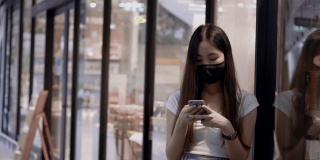 一名年轻女子戴口罩，在公共区域玩智能手机。