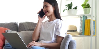 亚洲女性坐在家里用笔记本电脑工作，同时与客户交谈。