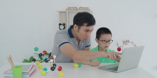 亚洲男孩学生与父亲视频会议电子学习与教师电脑学习在家里的科学教学。在家教育和远程学习，在线，教育和互联网。