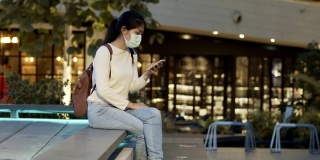 Asian woman wearing the face mask sitting and using smart phone in the park