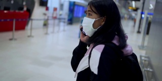 亚洲女性在机场航站楼主厅使用智能手机佩戴医用口罩，旅行导航系统应用，新冠肺炎大流行后，新常态社会距离概念，慢动作