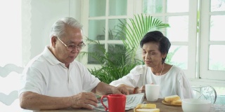 一对亚洲老夫妇在餐厅共进早餐。70多岁退休老人和女人一起看报，享受时光。