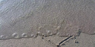 画在沙滩上的心的形状，被轻柔的海浪冲走。海上度假。一个爱情故事的概念和一个浪漫的假期。