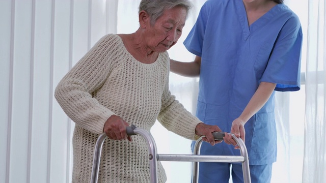 亚洲女性护理人员，帮助亚洲老年妇女在家或医院步行训练和康复过程。老祖母倾听照顾者给予的支持，老年人医疗保健，物理治疗