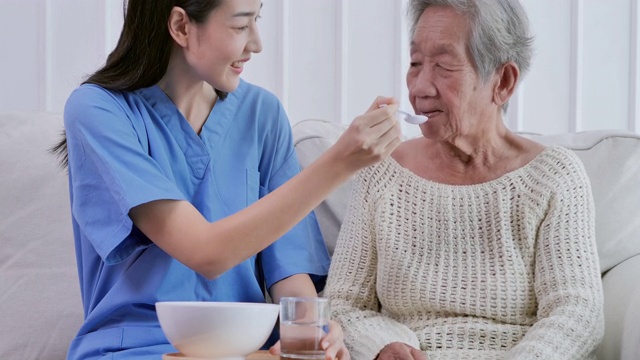 亚洲年轻女性护理护士帮助喂早餐病人亚洲老祖母82岁在养老院。