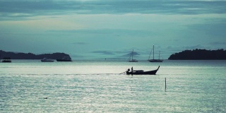 黎明时分，一名泰国男子在长尾船上捕鱼