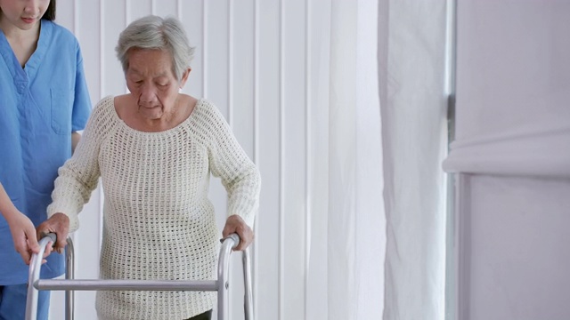 亚洲女护士医生，帮助82岁的亚洲老年妇女在家或医院步行训练和康复过程。老祖母倾听照顾者给予的支持，老年人医疗保健，物理治疗。在家里照顾者
