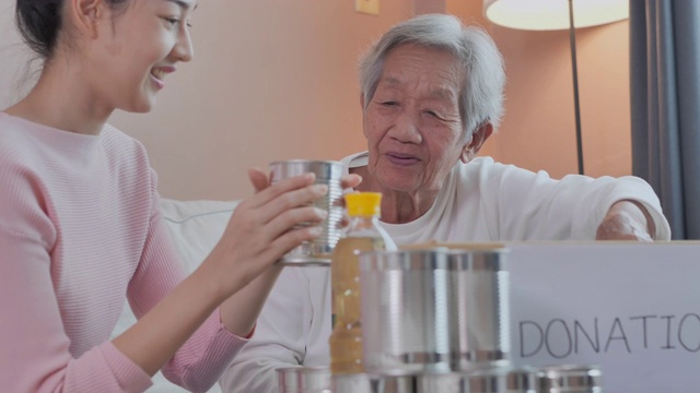 幸福的亚洲家庭，年老的老妇人和女儿把食物和饮料装进家里的捐赠箱，为COVID-19期间无家可归的人捐赠。东南亚及东亚:50岁以上人士