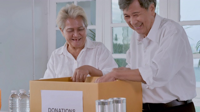 快乐的亚洲夫妇资深志愿者打包食物和饮料到捐赠盒在家里，为无家可归的人在COVID-19期间捐赠。东南亚及东亚:50岁以上人士