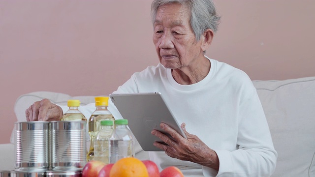 65岁以上的亚洲老年妇女使用科技平板电脑，在日常生活中轻松和自信地查看网上购物。技术，社会联系，网上购物，老年人购物，退休，技术精明的老年人
