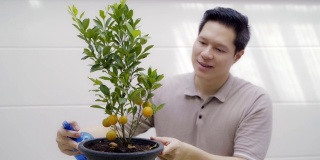 年轻的亚洲男子在家里用幸福浇灌花盆里的橙树。