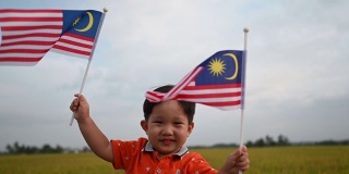 马来西亚独立日，一个亚洲华人小男孩在帕迪球场挥舞着马来西亚国旗，享受着清晨的阳光，感到自豪和快乐
