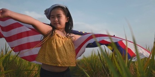 马来西亚独立日当天，一名亚洲华裔女孩身披马来西亚国旗，在帕迪球场享受清晨的阳光，感到自豪和快乐