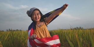 马来西亚独立日当天，一名亚洲华裔女孩身披马来西亚国旗，在帕迪球场享受清晨的阳光，感到自豪和快乐