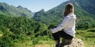 白种女游客坐在山顶的边缘，看自然和风景的山