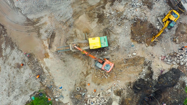 正在拆除建筑物现场工作的挖掘机。将水泥渣装进破碎设备，卡车运土磨石，高空俯视。