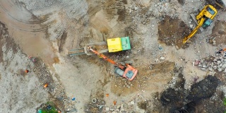 正在拆除建筑物现场工作的挖掘机。将水泥渣装进破碎设备，卡车运土磨石，高空俯视。