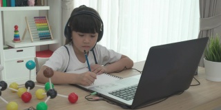 亚洲女学生视频会议电子学习科学课与老师和同学在家里的客厅电脑上。在家教育和远程学习，在线，教育和互联网。
