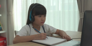 亚洲女学生视频会议电子学习与老师和同学在电脑上在家里的客厅。在家教育和远程学习，在线，教育和互联网。