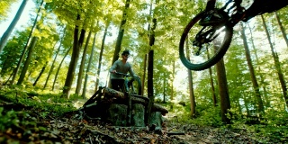 超级SLO MO MTB摩托车手跳过一个木斜坡在阳光明媚的森林