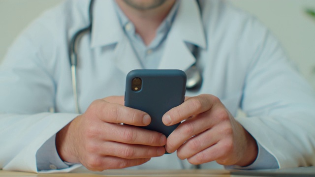 穿着白大褂的男医生使用带有触摸屏的现代智能手机。医生使用手机向患者发送短信，告知医疗检查结果。
