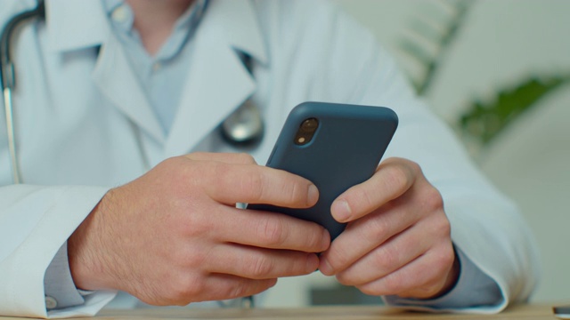 穿着白大褂的男医生使用带有触摸屏的现代智能手机。医生使用手机向患者发送短信，告知医疗检查结果。